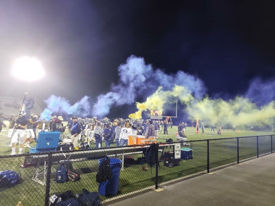 Varsity+Football+runs+onto+the+Kellam+football+field+at+kickoff+with+blue+and+yellow+colored+smoke+sticks.+The+visual+effect+earned+lots+of+cheer+from+the+audience.+Nov.+9%2C+2018.
