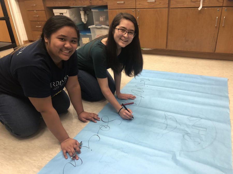 NHS community service chair Isabel Motil (left) and general assembly member Mariko Hart (right) add details to a banner for the winter social on Dec. 6.