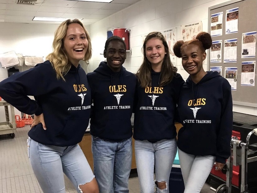 Trainers Kacey Counts, Jalen Powell, Emily Dixon, and Izzy Carter pose in the training room before a football game. 