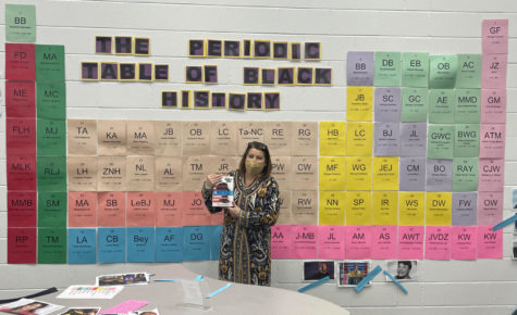 Library Media Specialist Nicole Glaser holds the book, Stamped, a New York Times Bestseller, and she stands in front of a periodic table display created for Black History Month on Feb. 24, 2022. 