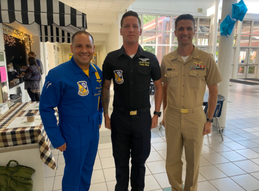 Lt. Henry Cedeño, Samuel Smith, and another Navy representative wait for students to exit auditorium in order to sign a complimentary Blue Angels poster. Each student who attended the assembly was given a colored poster that illustrated the Blue Angels flying over the Virginia Beach coastline.