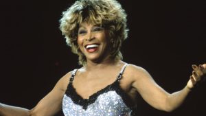 Tina Turner passionately sings on stage in her classic punk hairdo and stunning silver dress. She sported this look during the “Wildest Dreams Tour” in 1997.  (Paul Bergen/Getty Images)
