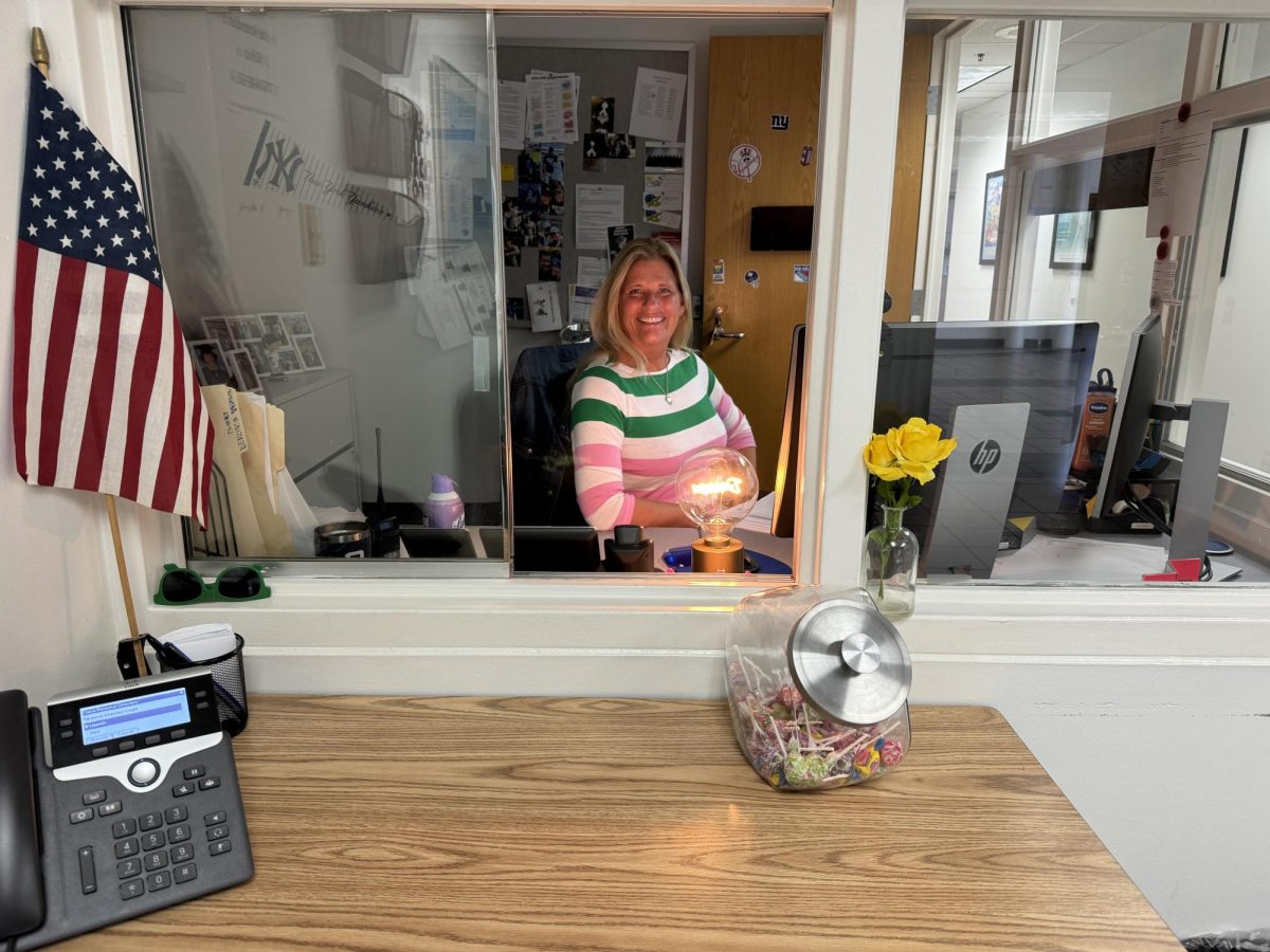 Attendance Secretary Genine Duffy smiles following a long line of morning attendance  check-ins on Oct. 18, 2024, in the attendance office. Displayed on the table is her popular candy jar.