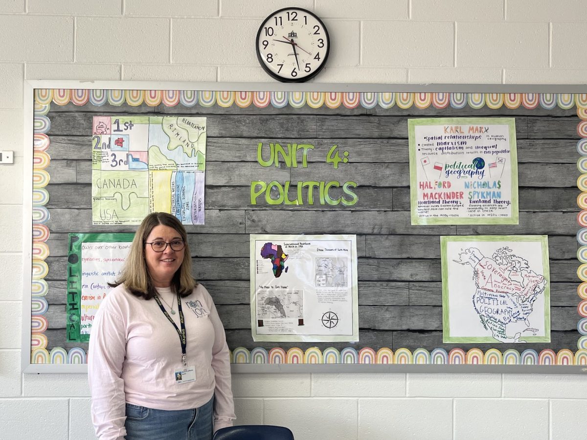 Stasia LaRoche proudly embraces artwork created by AP Human students for the politics unit four on Dec. 11, 2024, in Room 154. The students colored and labeled various maps. 
