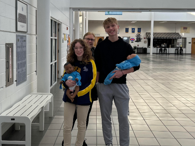 From left to right: senior Julia Swartzbaugh, family and consumer science teacher Carrie Jarvis and senior Cole Anderson hold their RealCare babies in the cafeteria foyer on Dec. 6, 2024. Students were allowed to take home their babies for two nights starting at the beginning of November.