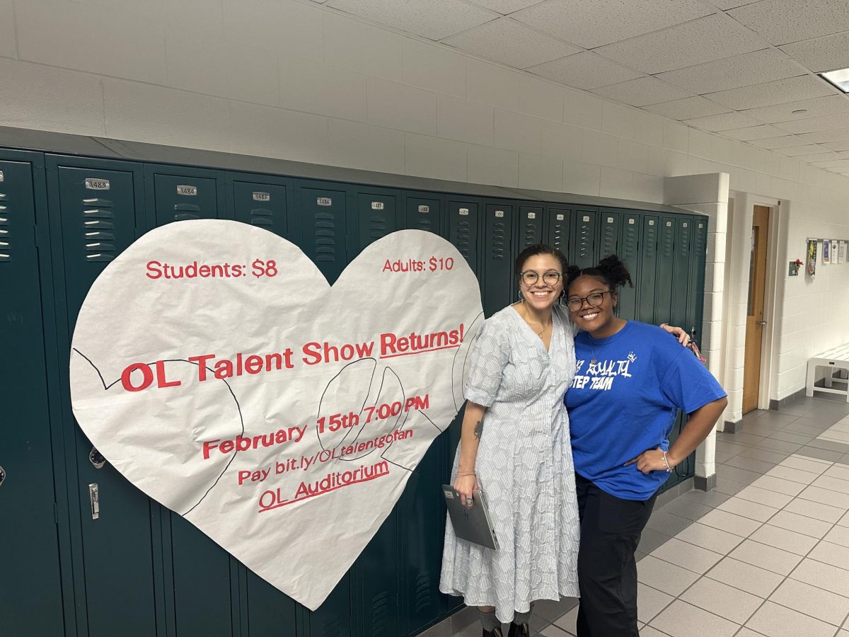 Step Team Coach Sarah Burford and Captain Tajyhia Manuel stand in the English hallway beside a poster advertising the upcoming talent show. The show will happen on Saturday, February 15, 2025. 