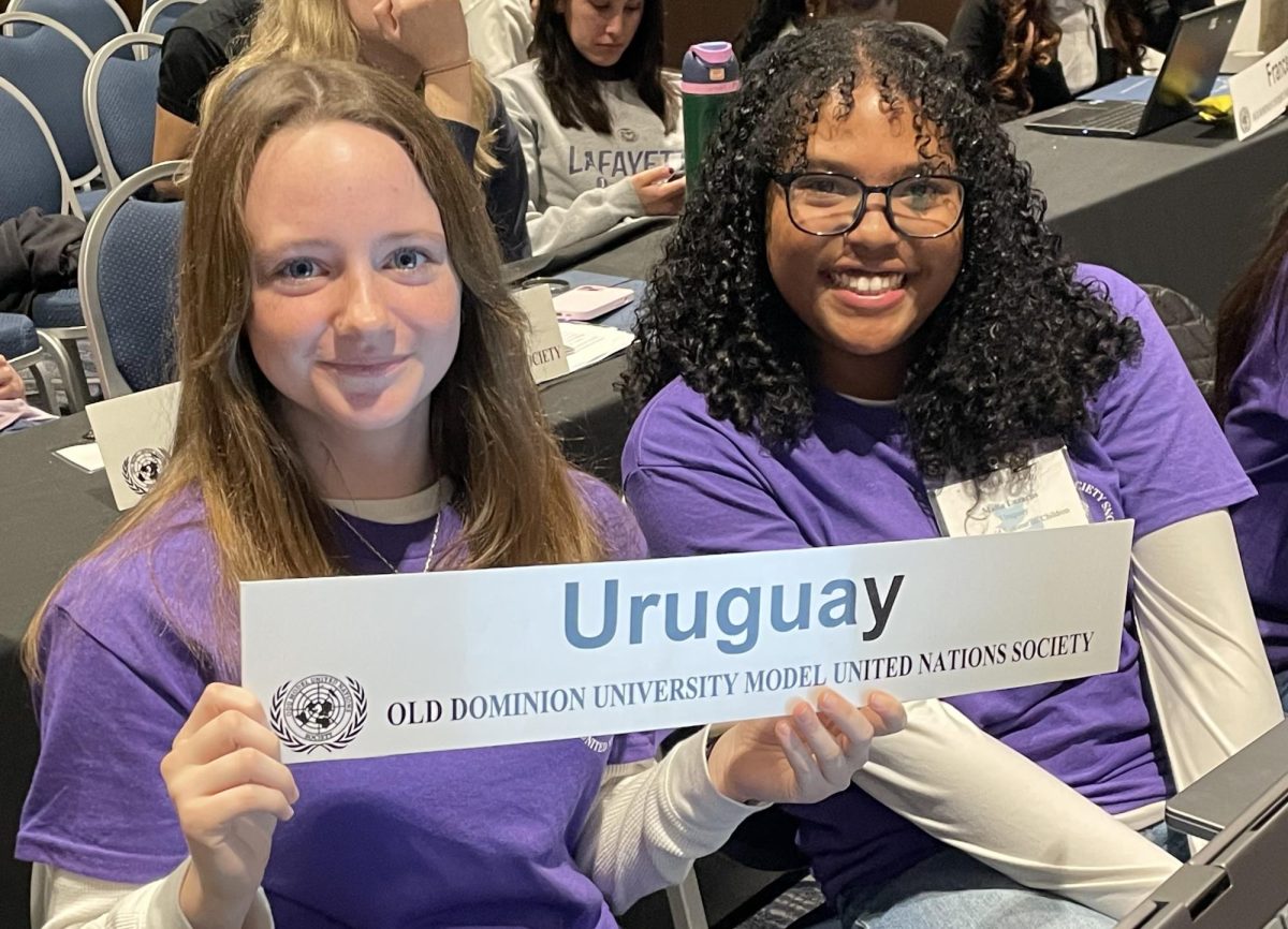 Senior Ava Sharp (left) and sophomore Malia Diaz (right) hold up their placards showcasing their country on Feb. 16, 2025. They were delegates of Uruguay for the General Assembly on the UN World Summit on Children. The delegates were allowed to wear purple shirts on the last day if they bought them rather than formal clothes. Photo used with permission from Lisa Gibson.