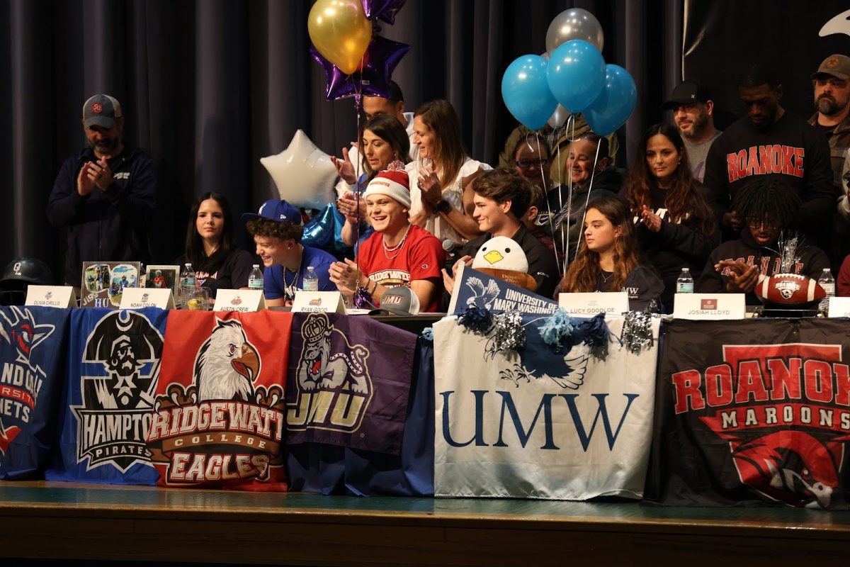 From left to right: seniors Olivia Cirillo, Noah Colon, Austin Crew, Ryan Gocio, Lucy Goodloe and Josiah Loyd celebrate after officially signing to continue their athletic career at the collegiate level on Feb. 5, 2025, in the auditorium at Ocean Lakes High School. Photo used with permission from Lauren Rakov.
