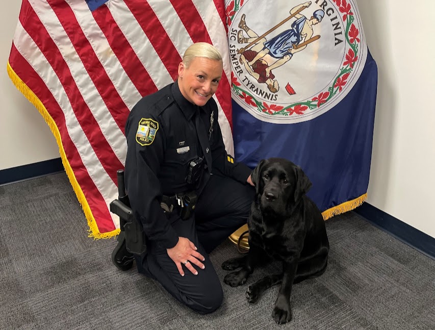 GiGi the English Labrador Retriever sits next to her handler MPO Johannessen in front of the American and state flags. Photo used with permission by MPO Nicole Johannesen.