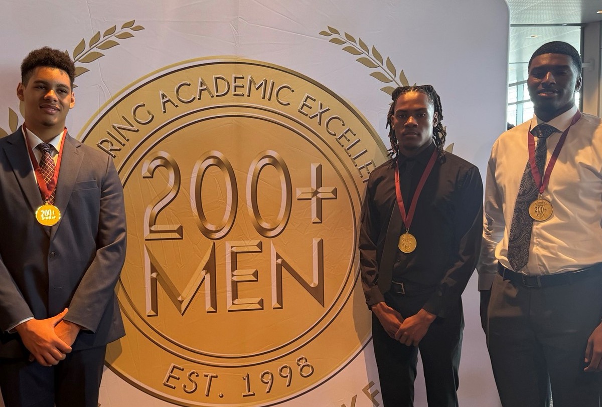 Seniors Derek Gross, ZayQuan Reynolds and Josiah Lloyd pose for a picture in front of a sign that has the symbol of the Men 200+. Photo taken on May 17, 2025. Photo used with permission by Michele Clark.