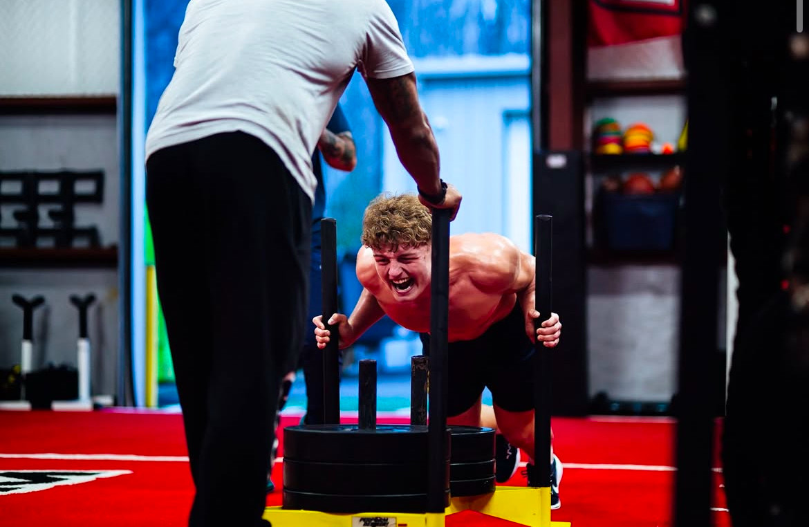 Photo captures linebacker Taylor Vogel doing sled pushes while TNDO trainer and gym owner Giavanni Ruffin pushes back. This photo was taken on March 12, 2025 during the Dolphin’s football workout. Photo used with permission by Giovanni Ruffin.