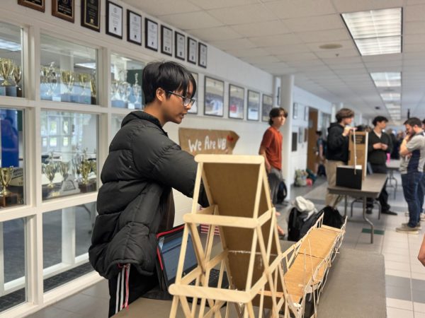 Sophomore Khai Ly demonstrates his project on March 24, 2026 on Academic Street. He used Popsicle sticks and cardboard to build his model, which ended up occupying an entire table.