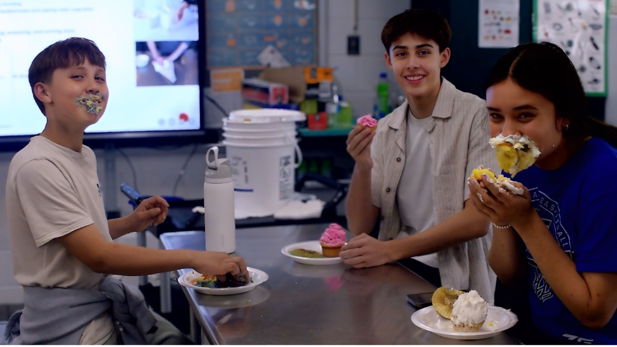 Pictured from left to right: Michael Holuka, freshman Haden Ramirez, and Farron Holuka smear frosting on their faces as they eat the cupcakes that they decorated in room 113. Micheal and Farron are the children of culinary teacher Brooks Holuka.