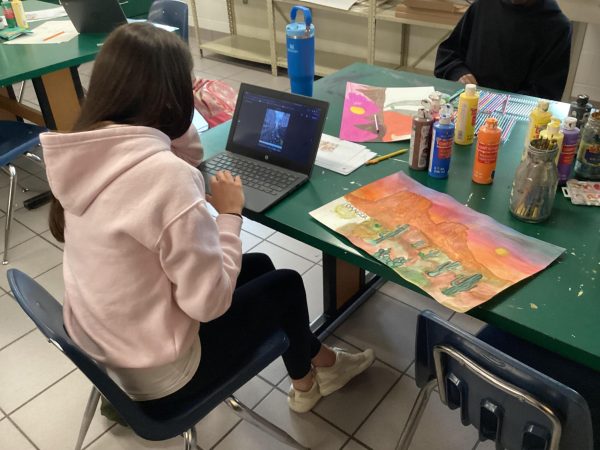 Sophomore Lily Wharton sitting in Art I Foundations after completing her artwork of a desert, which sits to her right, on Apr. 28. Creating pieces of art like this can give students an outlet for their own creativity, allowing them to express themselves.